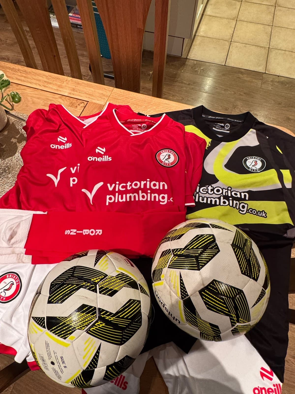 Donated Bristol City shirts, goalkeeper kit, shorts, socks and two footballs on a wooden table
